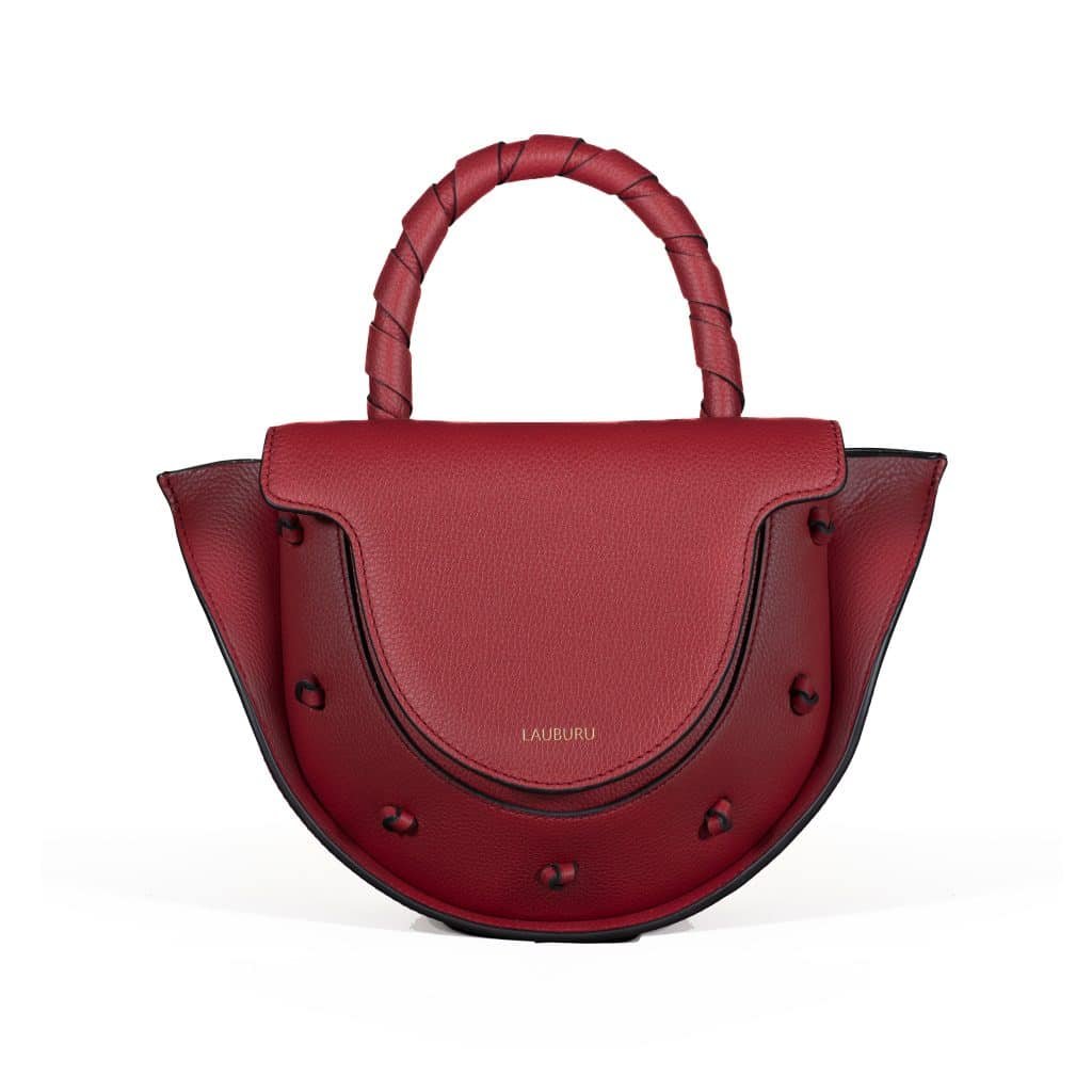 Bolso de piel burdeos Lauburu con asa trenzada y solapa estructurada. Diseño elegante con detalles anudados en contraste y logo grabado en dorado, ideal para un estilo sofisticado y exclusivo.